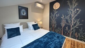A bedroom with a bed, a nightstand, a wall-mounted air conditioner, a framed picture, and a mural with trees and a moon. - Cozy lodge with SPA, pets allowed and parking (Saint-Léon)