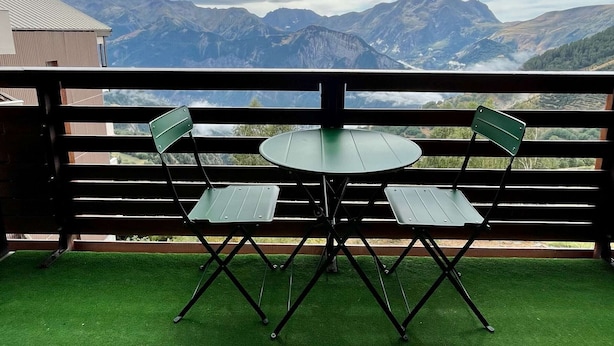A balcony with a table and chairs, overlooking a mountainous landscape.
