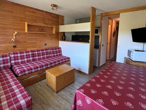 Una stanza accogliente con un divano rosso e bianco a scacchi, un tavolino in legno e un letto con copripiumino dal motivo rosso.