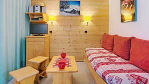 Une pièce chaleureuse avec un mur en bois, un lit avec une literie à motifs, une table avec une tasse rouge, un téléviseur et un cadre photo.