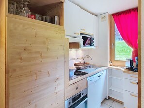 A compact kitchen with wooden cabinetry, a microwave, a sink, and a window with a red curtain.