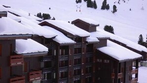 Un chalet à étages doté de balcons et d’un toit enneigé, entouré d’arbres et d’un paysage hivernal.
