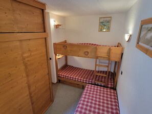 A bunk bed room with a wooden wardrobe, a small table, and a wall-mounted lamp.