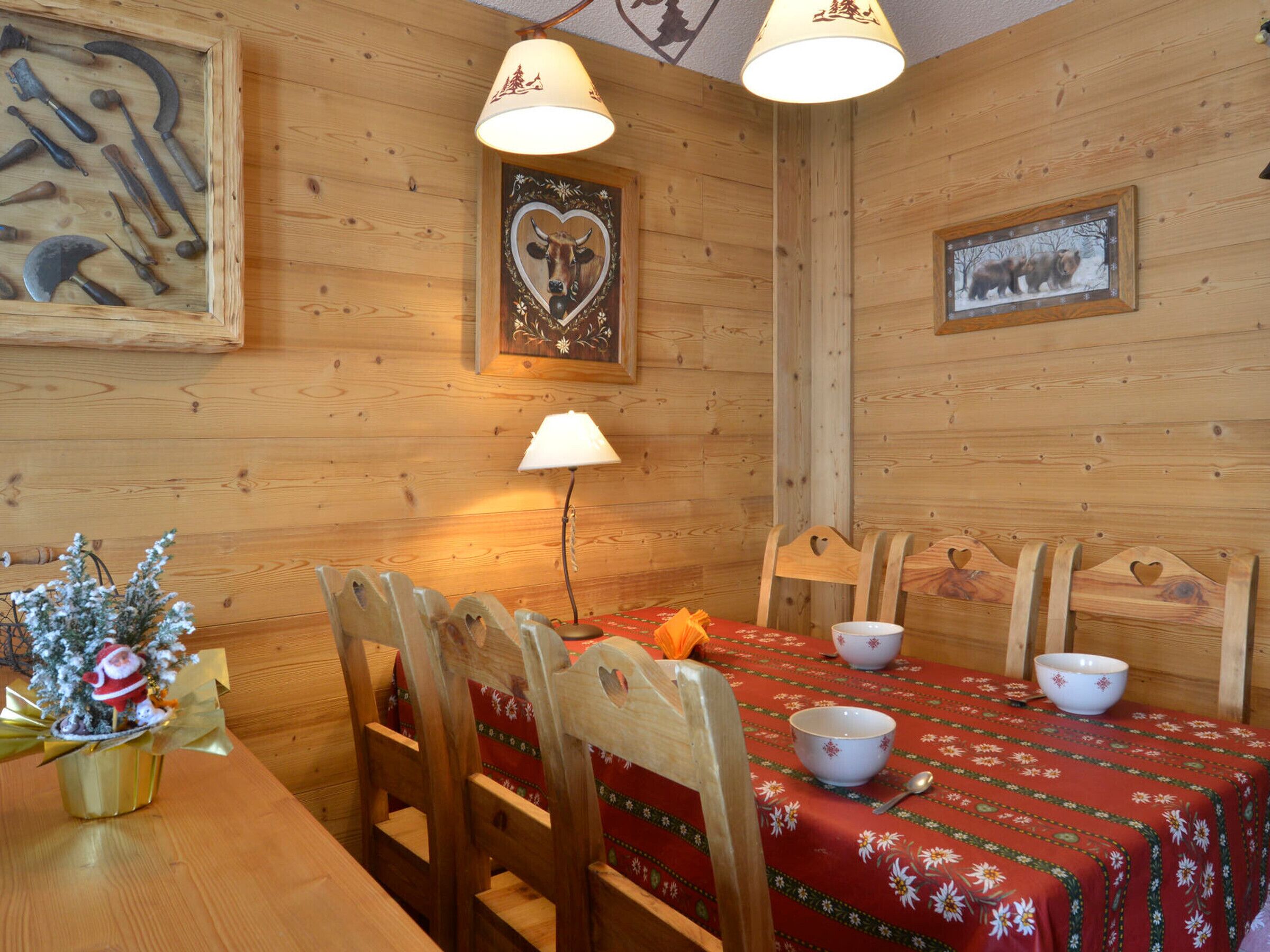 Interior de madera con una mesa de comedor dispuesta para cuatro personas, rodeada de sillas de madera con diseños de corazones.