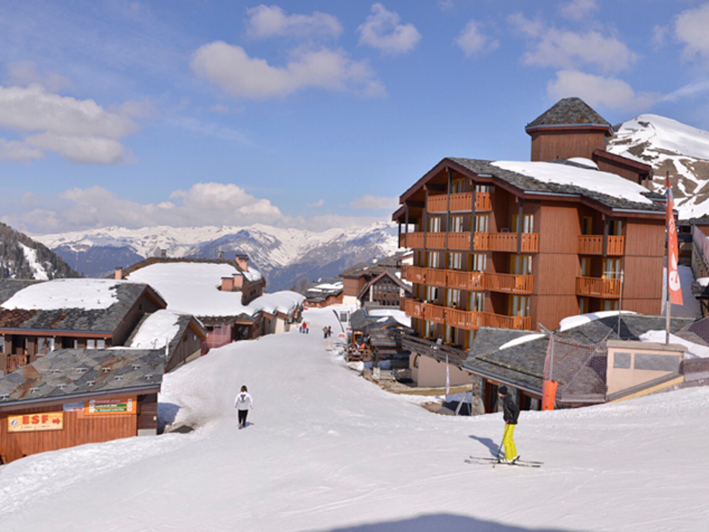 A snow-covered mountain village with wooden buildings, a ski slope, and a clear sky.