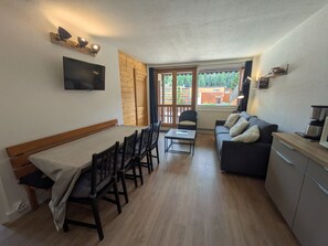 A compact living space with a dining area, a sofa, a TV, and a kitchenette.