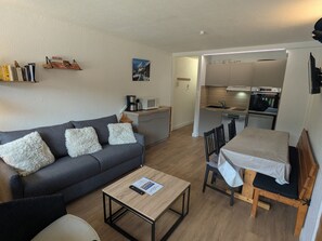 A compact living space with a sofa, a coffee table, a dining table with chairs, a kitchenette, and a small bookshelf. - Spacious apartment, mountain view - 7 guests (La Plagne)