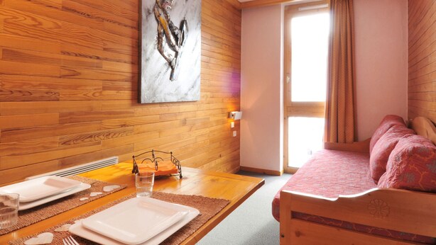 A wooden-paneled room with a dining table set for two, a bed with a pink bedspread, and a large abstract painting on the wall. - Comfortable divisible studio 4 pers, near slopes and shops (Plagne Bellecôte)