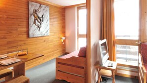 A wooden-paneled room with a bed, a desk with a laptop, a marble artwork, and a window with curtains. - Comfortable divisible studio 4 pers, near slopes and shops (Plagne Bellecôte)