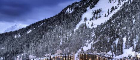 A snow-covered resort with multiple high-rise buildings, ski lifts, and a mountainous backdrop.