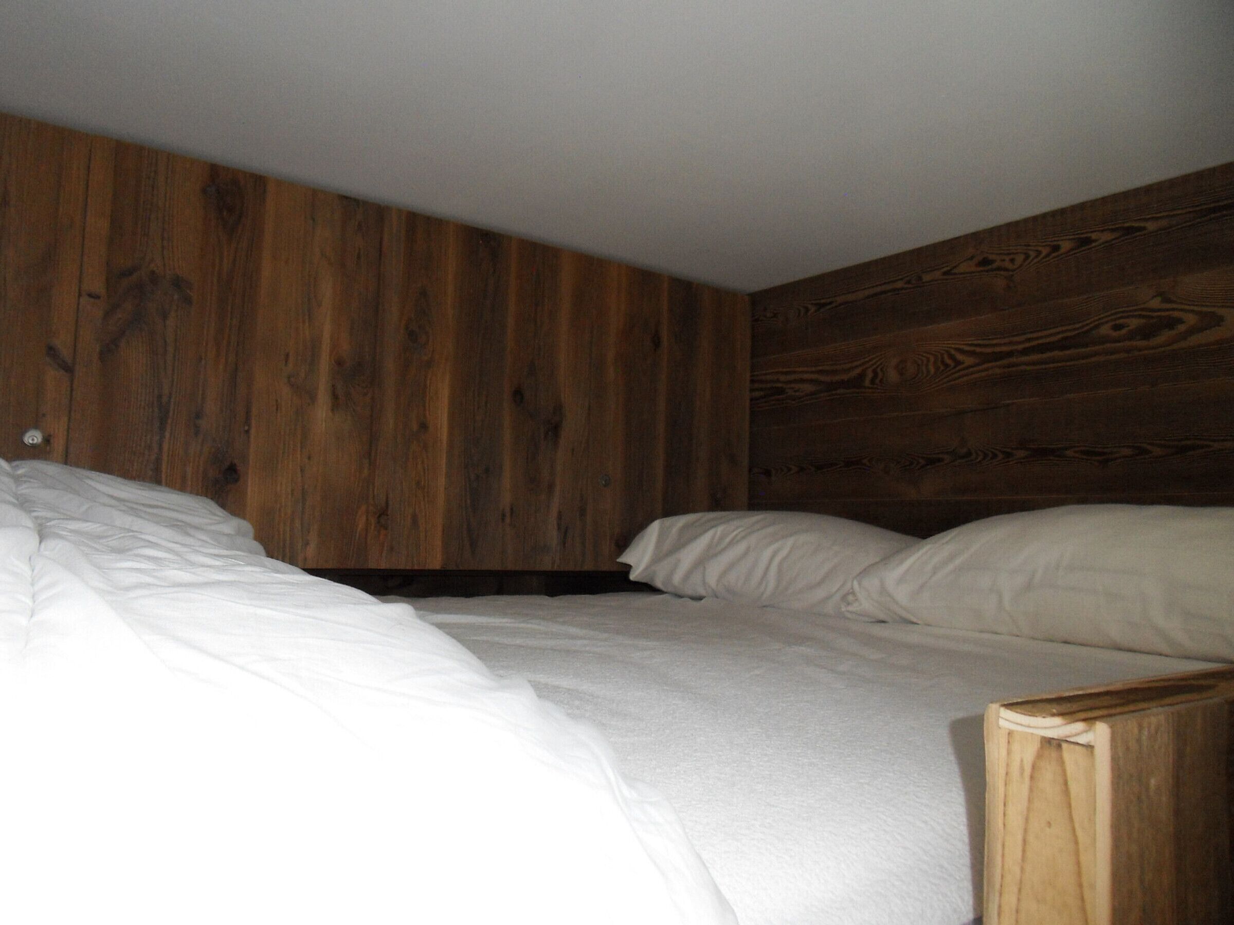 Une chambre avec deux lits, une tête de lit en bois et du linge de lit blanc.