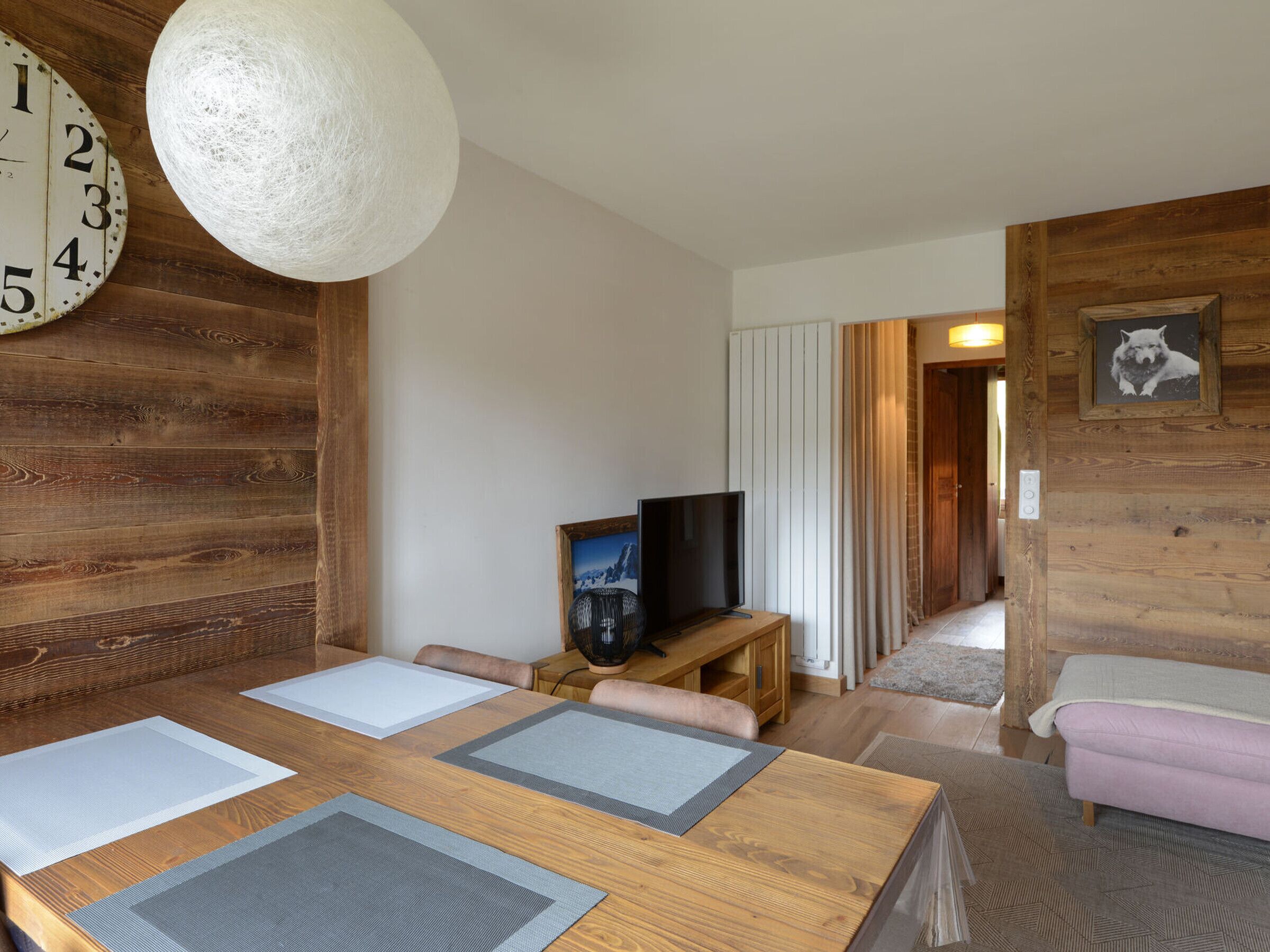 A wooden interior with a dining table, chairs, a television, and a clock.