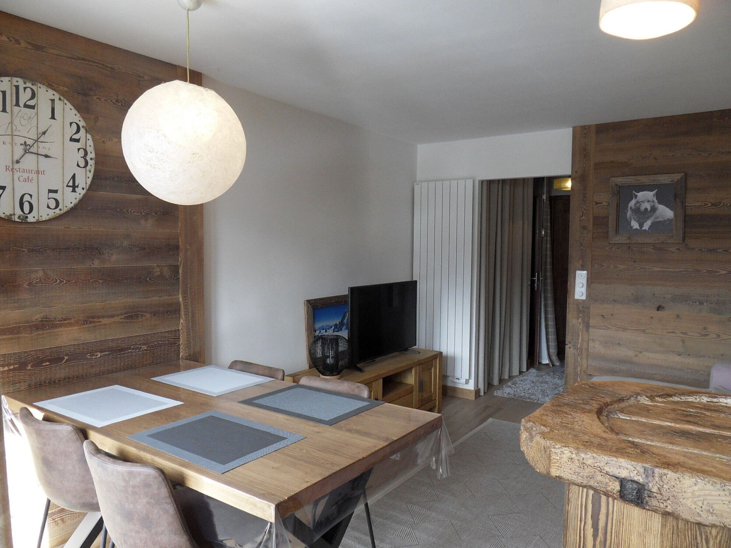 A dining area with a wooden table, chairs, and a large clock on the wall.