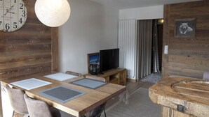 A dining area with a wooden table, chairs, and a large clock on the wall. - Apartment at Base of Slopes • 5 pers • Slope View (Belle Plagne)