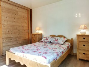 A bedroom with a wooden bed, two bedside tables with lamps, a wooden wardrobe, and a patterned bedspread.
