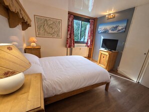 A bedroom with a bed, a wooden nightstand, a lamp, a television, and a window with curtains.