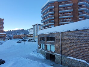 A snow-covered parking lot with a building featuring a stone facade and a wooden balcony.