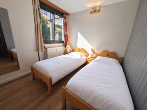 Un dormitorio con dos camas individuales, una ventana con cortinas, una mesita de noche con una lámpara y un radiador.