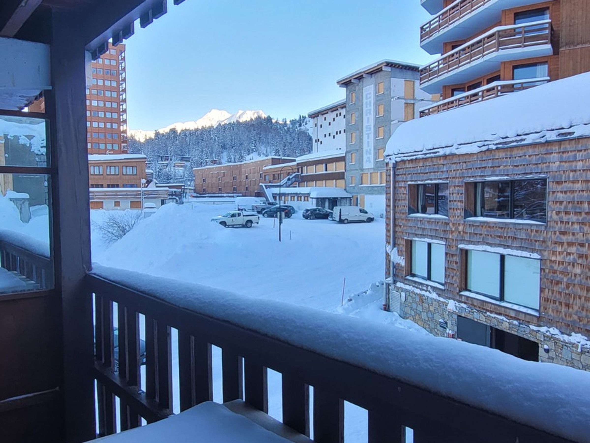 Quartiere residenziale innevato con edifici a più piani, cielo sereno e catena montuosa sullo sfondo.