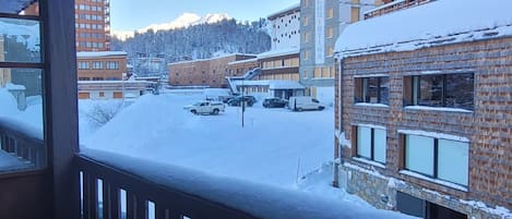 A snowy residential area with multi-story buildings, a clear sky, and a view of a mountain range in the background.
