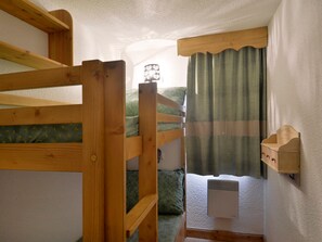 Un lit superposé avec une tête de lit, une table de chevet, une lampe et une fenêtre avec des rideaux.