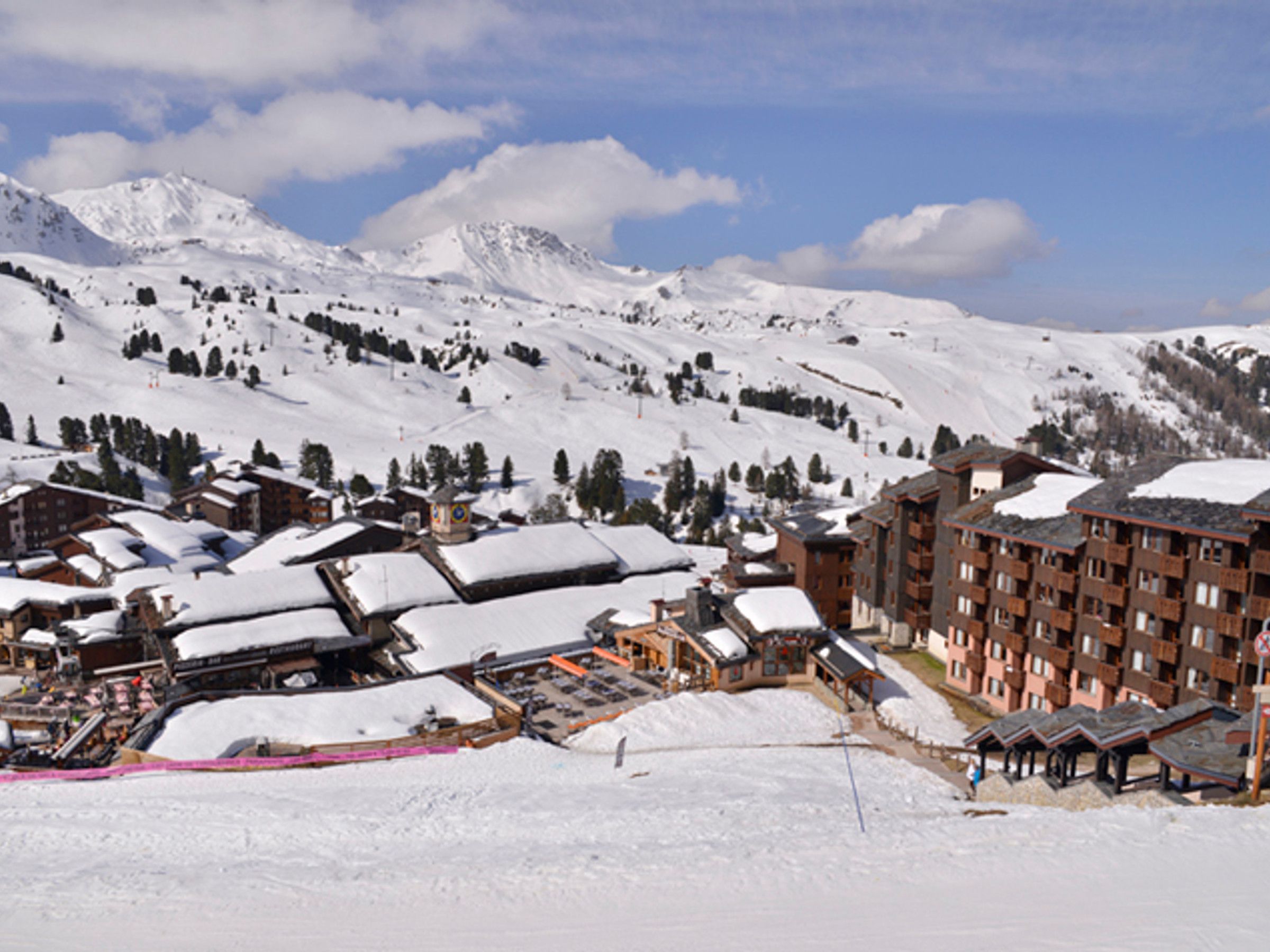 Uma cidade nas montanhas coberta de neve, com um grande hotel de vários andares e um teleférico visível ao fundo.