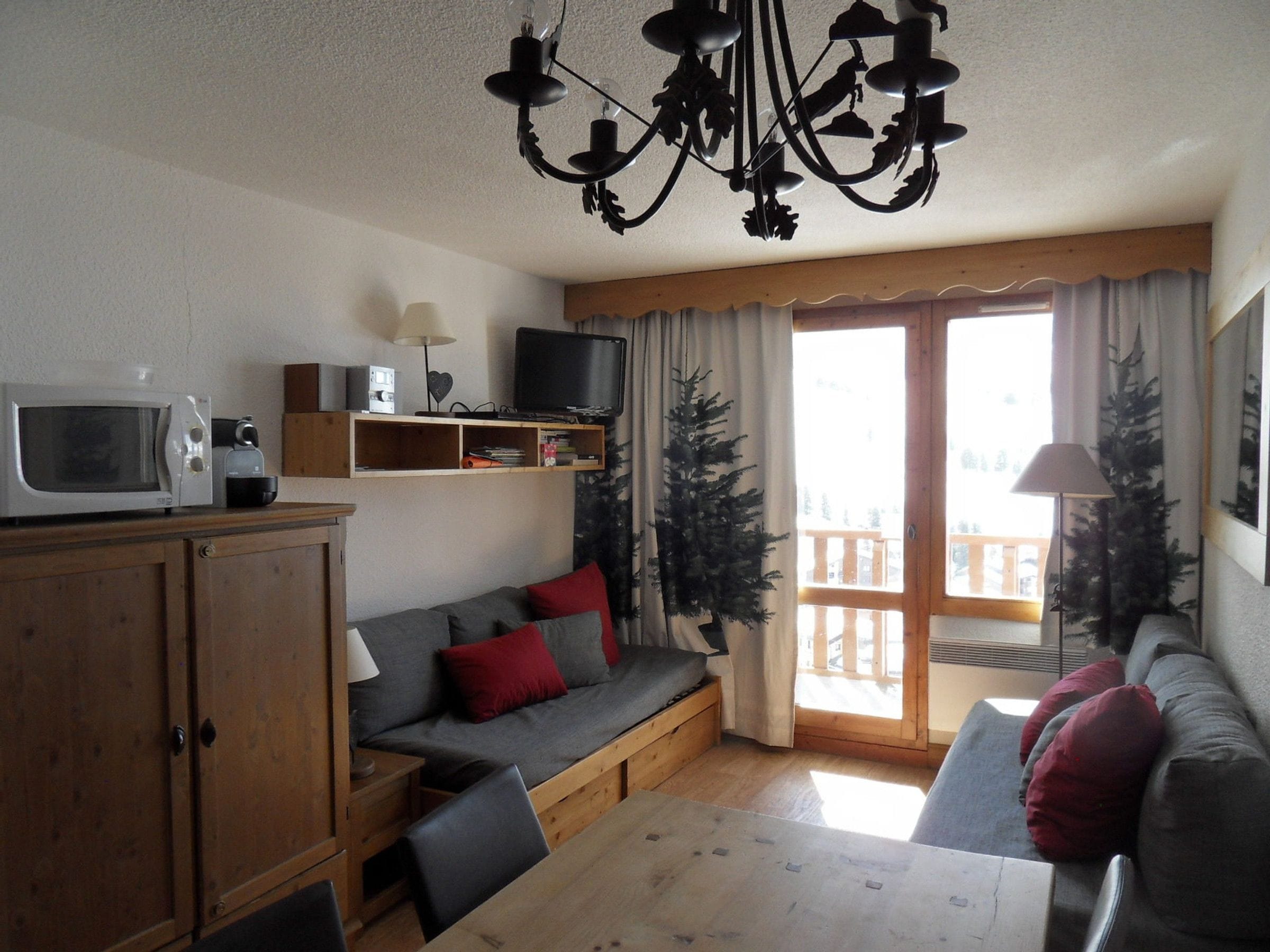 A cozy living room with a wooden table, a sofa, a television, and a ceiling light fixture.