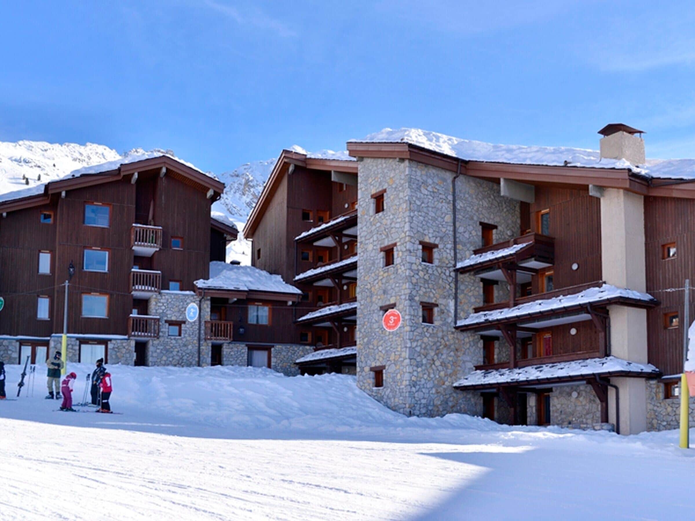 Ein mehrstöckiges Gebäude mit steinernen und hölzernen Fassaden, Balkonen und einer Skipiste im Vordergrund.
