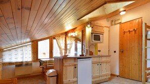 A cozy kitchen with wooden cabinets, a microwave, and a sink. There's a dining table with a magazine and a candle.