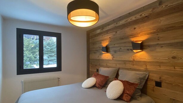 A bedroom with a bed, a window, a radiator, and wooden wall paneling.