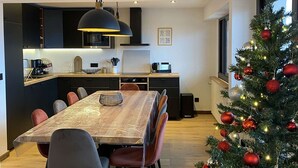 A modern kitchen with dark cabinetry, a dining area with a wooden table and chairs, and a decorated Christmas tree.