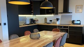A modern kitchen with dark cabinetry, a wooden dining table, and pendant lighting.