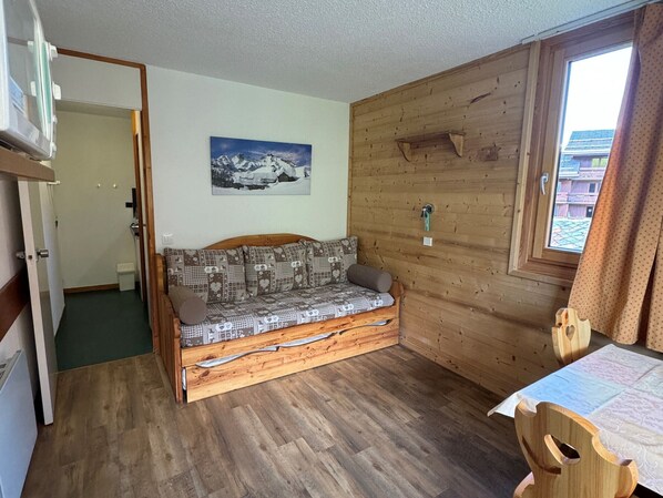 Une pièce chaleureuse avec un plancher en bois, un canapé agrémenté de coussins à motifs, un tableau au mur et une fenêtre avec des rideaux.