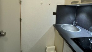A compact bathroom with a sink, a mirror, and a small trash bin.