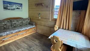 A cozy room with a wooden wall, a sofa, a table, and a window with curtains.