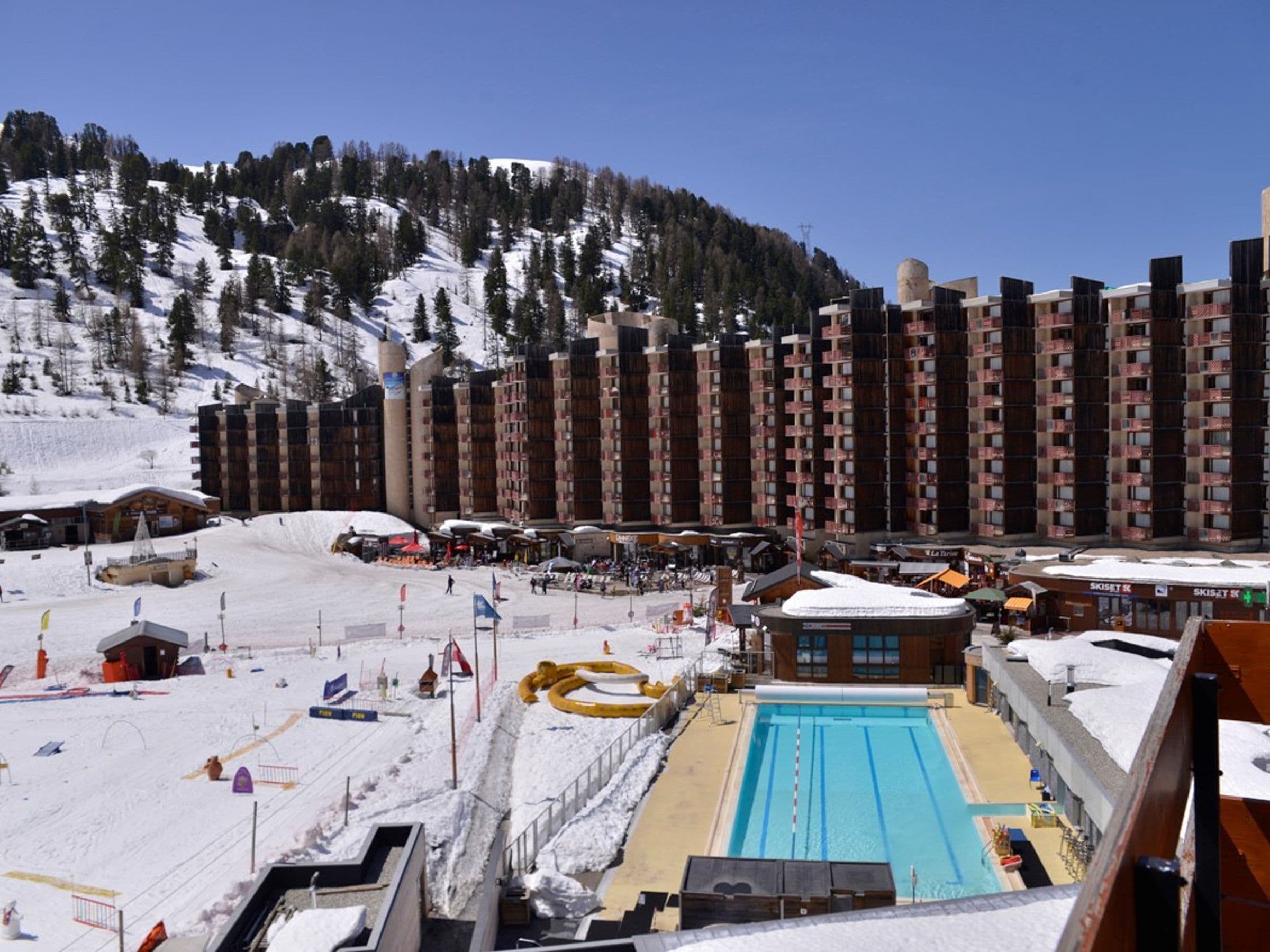 A ski resort with a swimming pool, ski lifts, and buildings with balconies.