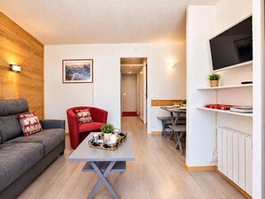 A compact living space with a sofa, a red armchair, a coffee table with decorative items, a television, and a dining area.