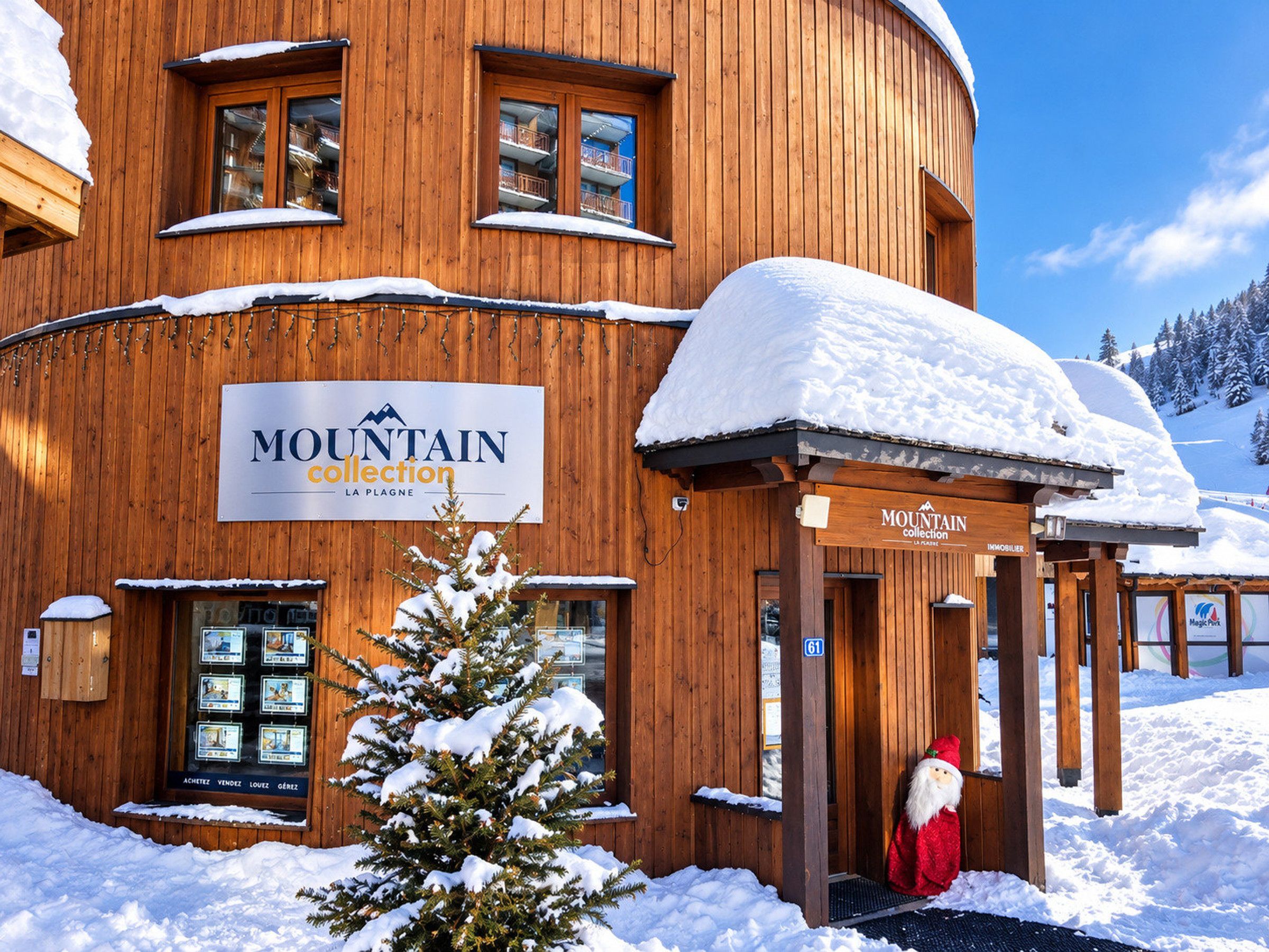 Puinen rakennus, jonka yläpuolella on kyltti, jossa lukee ”MOUNTAIN collection LA PLAGNE”, ja sen edessä on pieni joulukuusi.
