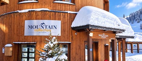 A wooden building with a sign reading 'MOUNTAIN collection LA PLAGNE' and a small Christmas tree in front.