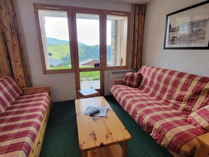 A room with a large window, a wooden table, two striped sofas, and a framed picture on the wall.
