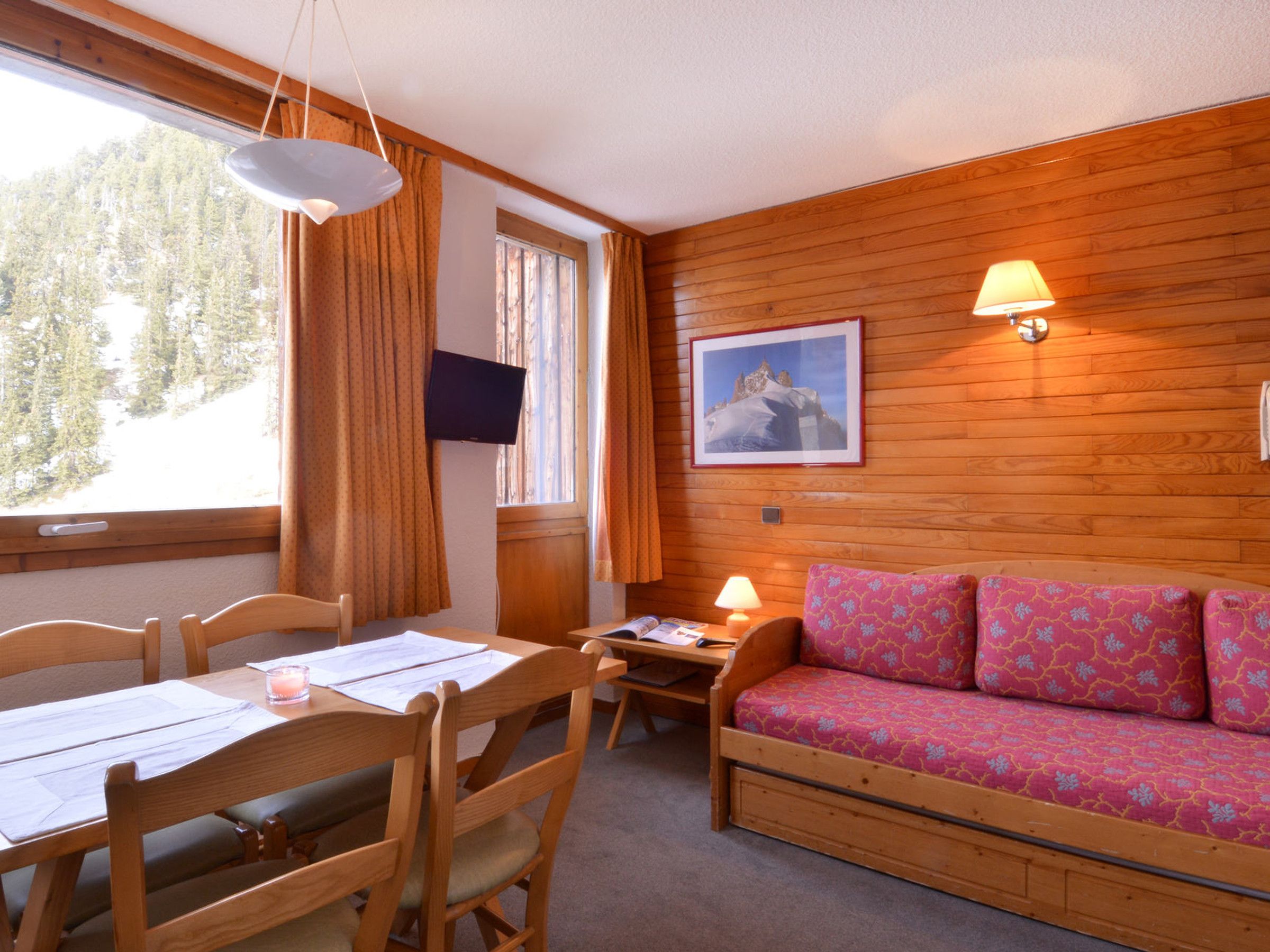 A cozy room with a wooden interior, a sofa with patterned cushions, a desk with papers, and a television on the wall.