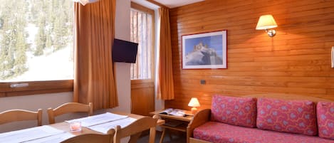 A cozy room with a wooden interior, a sofa with patterned cushions, a desk with papers, and a television on the wall.