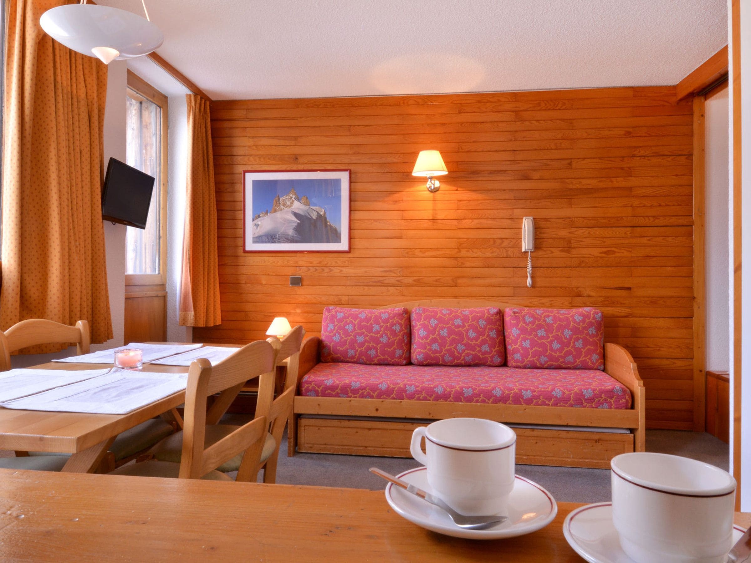 A cozy room with wooden walls, a sofa, a table with cups and a spoon, and a TV on the wall.