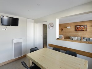 Una sala de reuniones moderna con una mesa de madera, sillas negras, un televisor montado, un radiador y una pared de madera con un reloj y un cuadro enmarcado.