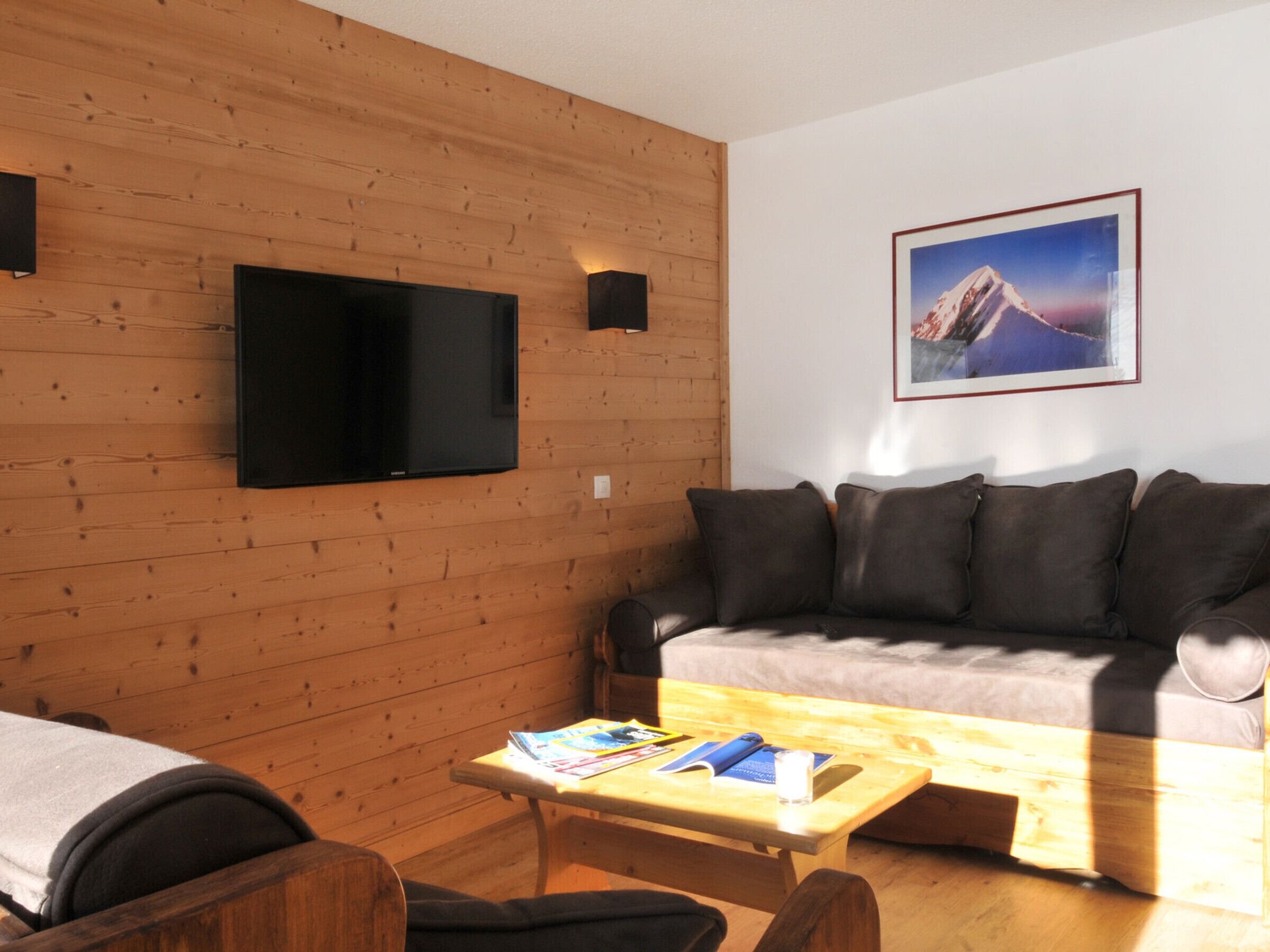 Une pièce chaleureuse avec un mur en bois, un téléviseur à écran plat, un canapé et une petite table sur laquelle se trouvent des livres et un verre.