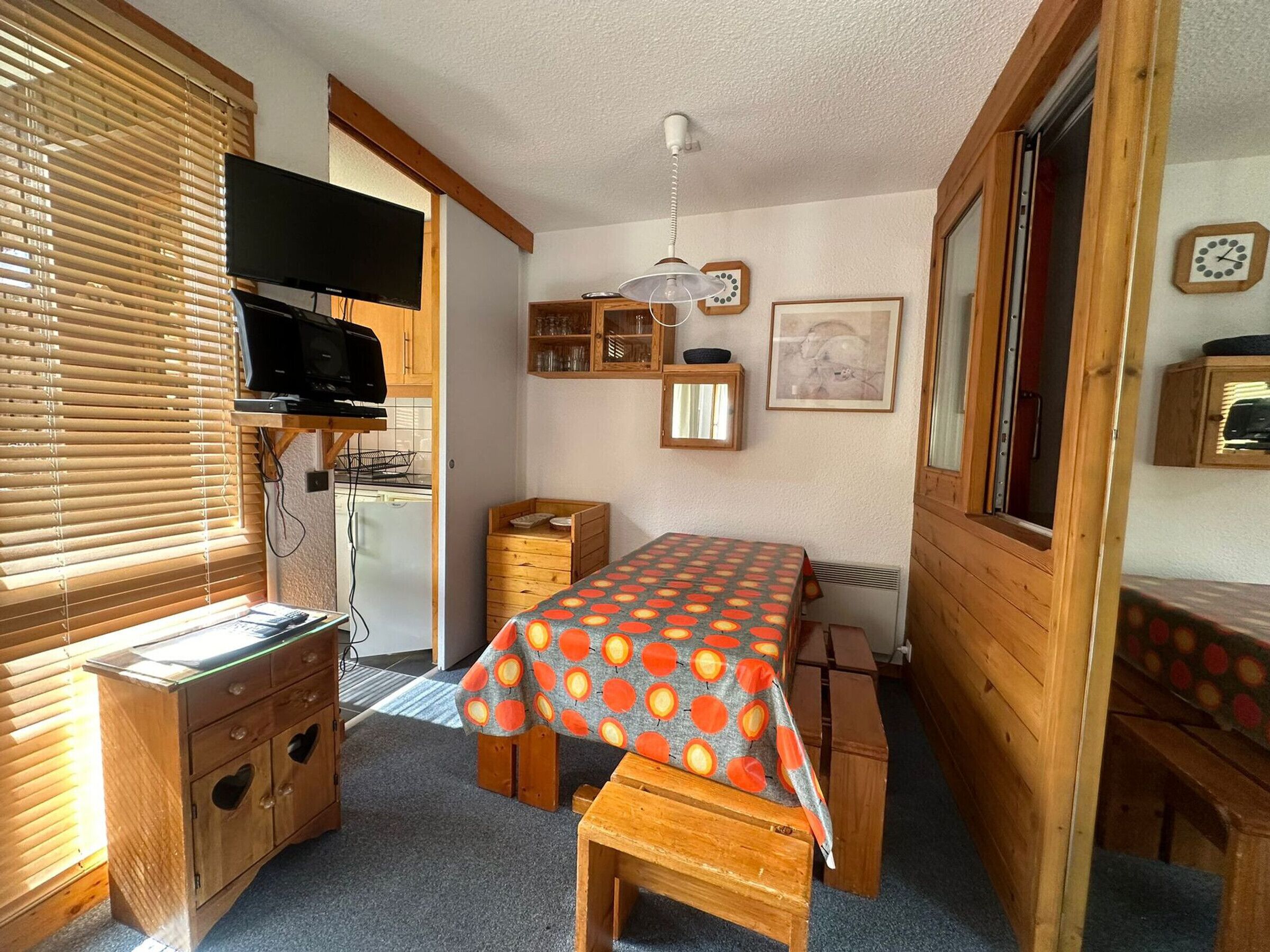 Ein kleines Zimmer mit Bett, Schreibtisch, Fernseher und einer Küchenzeile.