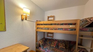 A bunk bed room with a desk and drawers, a small shelf with a lamp, and a framed picture on the wall.
