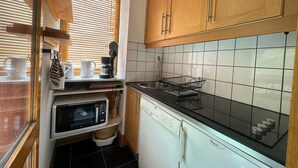 A compact kitchen with wooden cabinets, a microwave, a dishwasher, and a window with blinds.