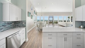 A spacious kitchen with white cabinetry, a large island, and a view of the ocean. - Beachfront Bliss: Spacious Deck, Grill & Unmatched Gulf Views! (Panama City Beach)