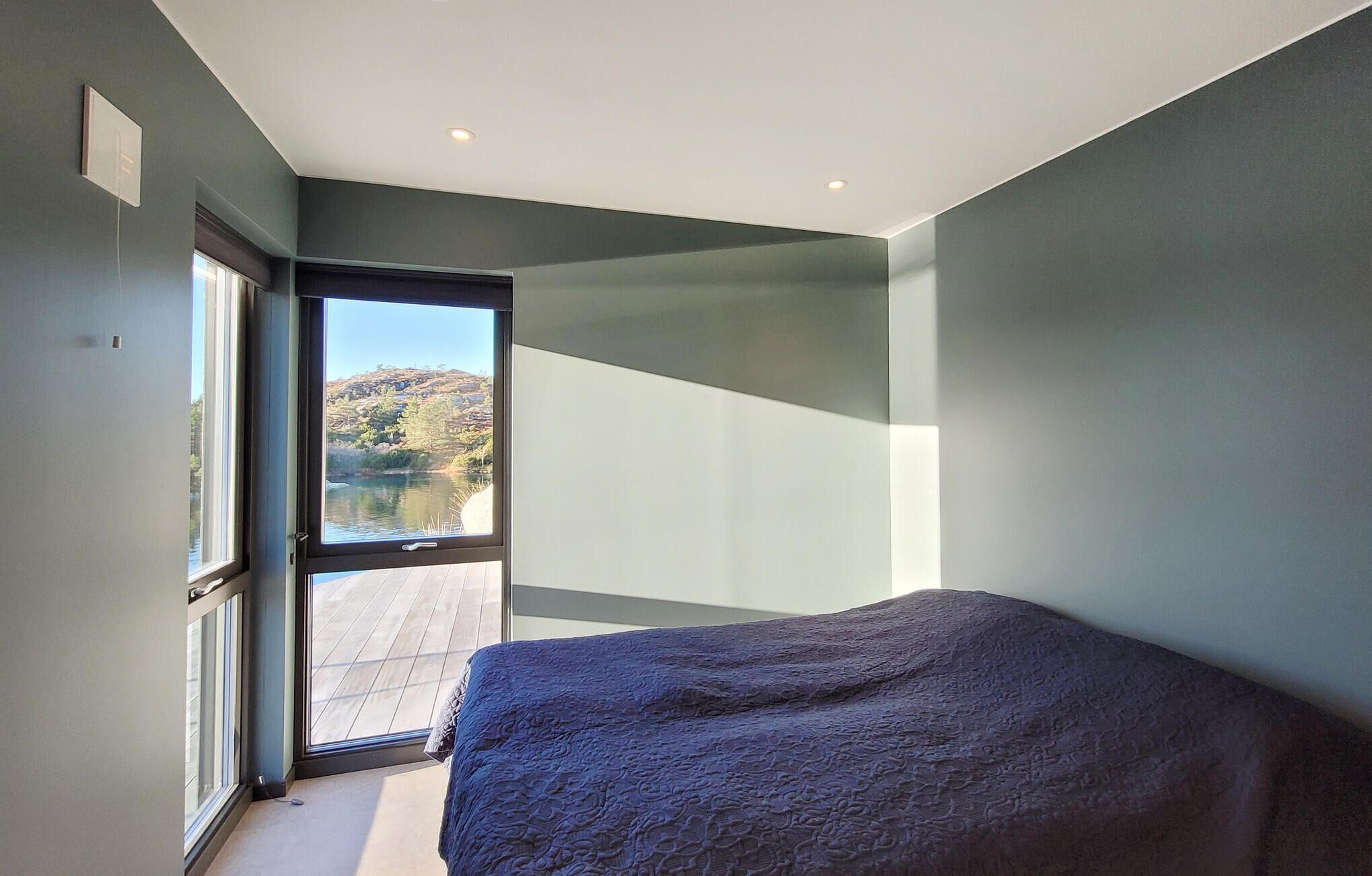 Un dormitorio con una cama grande, un ventanal corredero que da a un balcón y vistas a un lago y colinas.